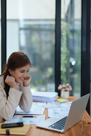 Confident business woman smiling Show successful gestures at her desk with market charts and documents in office.の写真素材