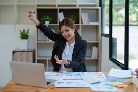 Confident business woman smiling Show successful gestures at her desk with market charts and documents in office.の写真素材