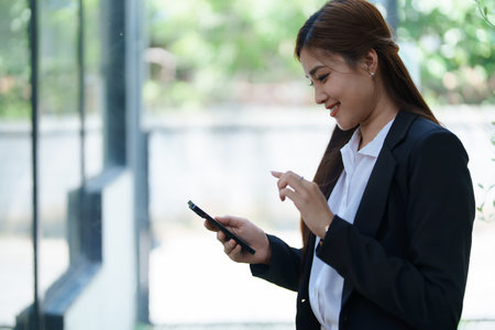Professional businesswoman engaged in smartphone call to calculate finance with using stock marketing charts, notebook, and laptop in office.の写真素材