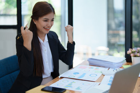 Confident business woman smiling Show successful gestures at her desk with market charts and documents in office.の写真素材