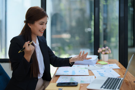 Confident business woman smiling Show successful gestures at her desk with market charts and documents in office.の写真素材