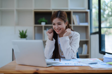 Confident business woman smiling Show successful gestures at her desk with market charts and documents in office.の写真素材