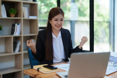 Confident business woman smiling Show successful gestures at her desk with market charts and documents in office.の写真素材