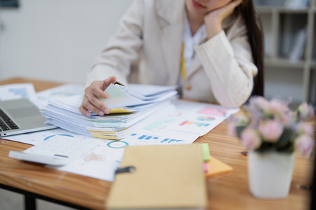 Stressed young businesswoman overwhelmed by paperwork with finance, market charts and documents in office.の写真素材