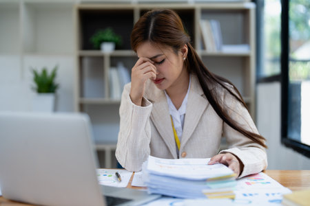 Stressed young businesswoman overwhelmed by paperwork with finance, market charts and documents in office.の写真素材