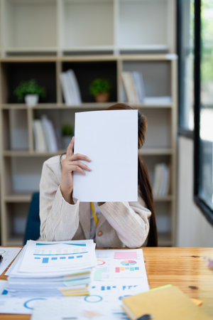 Stressed young businesswoman overwhelmed by paperwork with finance, market charts and documents in office.の写真素材