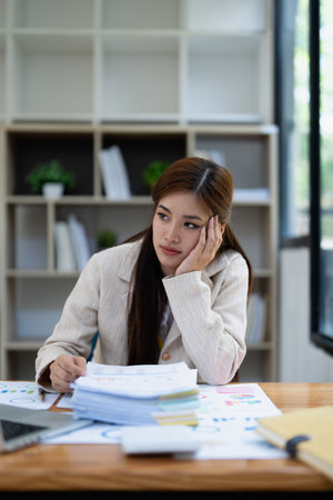 Stressed young businesswoman overwhelmed by paperwork with finance, market charts and documents in office.の写真素材