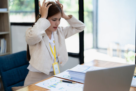 Stressed young businesswoman overwhelmed by paperwork with finance, market charts and documents in office.の写真素材