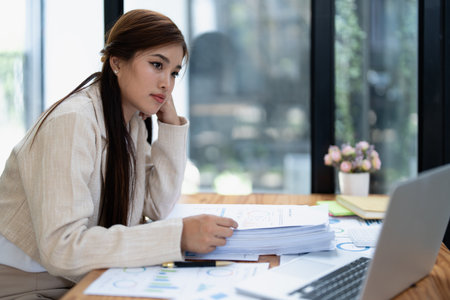 Stressed young businesswoman overwhelmed by paperwork with finance, market charts and documents in office.の写真素材
