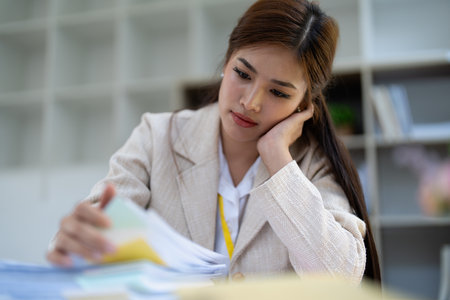 Stressed young businesswoman overwhelmed by paperwork with finance, market charts and documents in office.の写真素材
