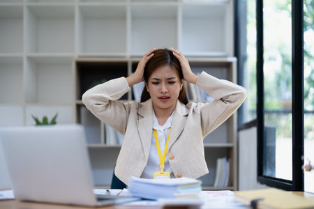 Stressed young businesswoman overwhelmed by paperwork with finance, market charts and documents in office.の写真素材