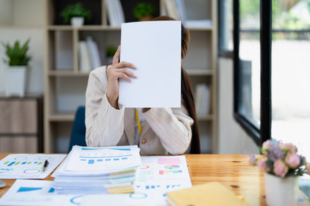 Stressed young businesswoman overwhelmed by paperwork with finance, market charts and documents in office.の写真素材