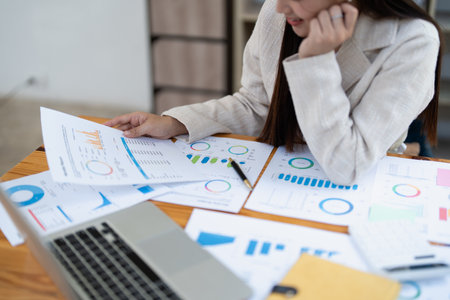 Confident business woman smiling Show successful gestures at her desk with market charts and documents in office.の写真素材