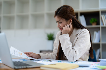 Confident business woman smiling Show successful gestures at her desk with market charts and documents in office.の写真素材