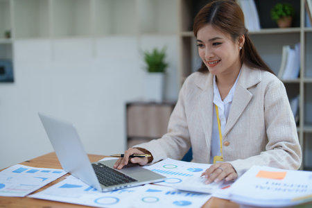 professional businesswoman planning and analyzing marketing charts and financial documents with a laptop and calculator papers on the desk.の写真素材