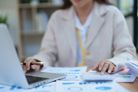professional businesswoman planning and analyzing marketing charts and financial documents with a laptop and calculator papers on the desk.の写真素材