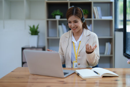 Asian businesswoman wears a headset while participation in an online video conference discussing marketing and finance strategies effectively.の写真素材