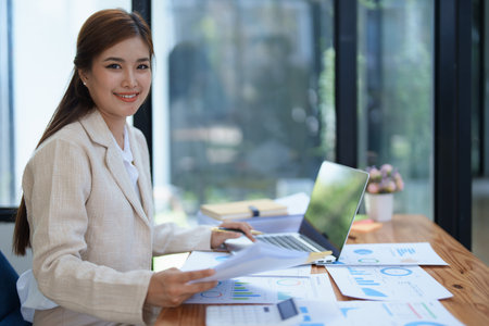 professional businesswoman planning and analyzing marketing charts and financial documents with a laptop and calculator papers on the desk.の写真素材
