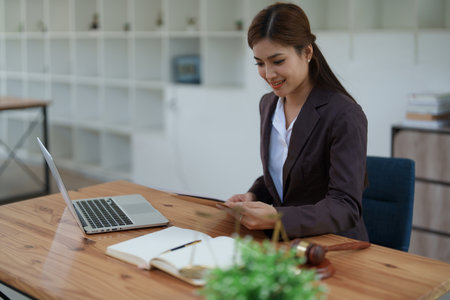 female attorney advisor at a law firm reviews legal documents at her desk equipped with a laptop notebook and scales of justice in the office.の写真素材