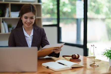 female attorney advisor at a law firm reviews legal documents at her desk equipped with a laptop notebook and scales of justice in the office.の写真素材