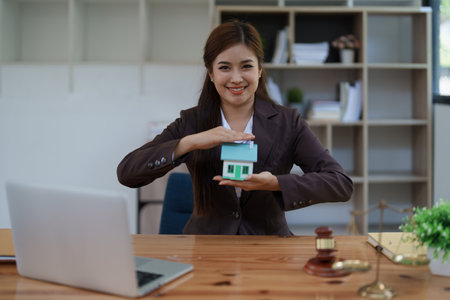 attorney woman at a desk with a laptop, miniature house, and gavel symbolizing real estate protection, home insurance, and property security services.の写真素材