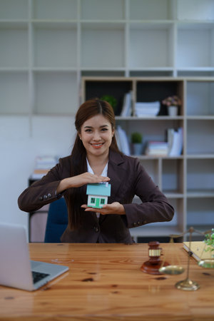 attorney woman at a desk with a laptop, miniature house, and gavel symbolizing real estate protection, home insurance, and property security services.の写真素材