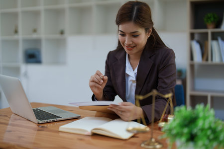 female attorney advisor at a law firm reviews legal documents at her desk equipped with a laptop notebook and scales of justice in the office.の写真素材