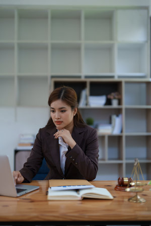 female attorney advisor at a law firm reviews legal documents at her desk equipped with a laptop notebook and scales of justice in the office.の写真素材