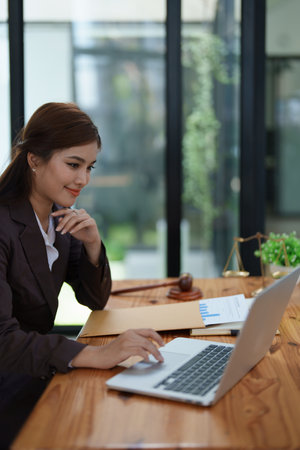 female attorney advisor at a law firm reviews legal documents at her desk equipped with a laptop notebook and scales of justice in the office.の写真素材