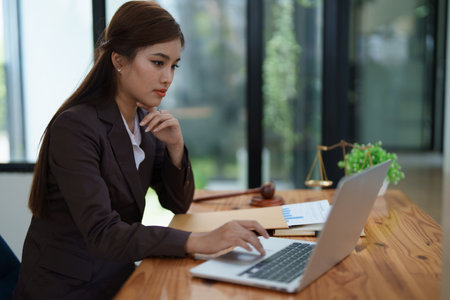 female attorney advisor at a law firm reviews legal documents at her desk equipped with a laptop notebook and scales of justice in the office.の写真素材