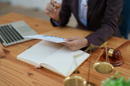 female attorney advisor at a law firm reviews legal documents at her desk equipped with a laptop notebook and scales of justice in the office.の写真素材