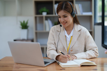 Asian businesswoman wears a headset while participation in an online video conference discussing marketing and finance strategies effectively.の写真素材