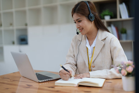 Asian businesswoman wears a headset while participation in an online video conference discussing marketing and finance strategies effectively.の写真素材