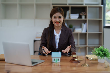 attorney woman at a desk with a laptop, miniature house, and gavel symbolizing real estate protection, home insurance, and property security services.の写真素材