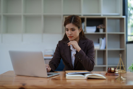 female attorney advisor at a law firm reviews legal documents at her desk equipped with a laptop notebook and scales of justice in the office.の写真素材
