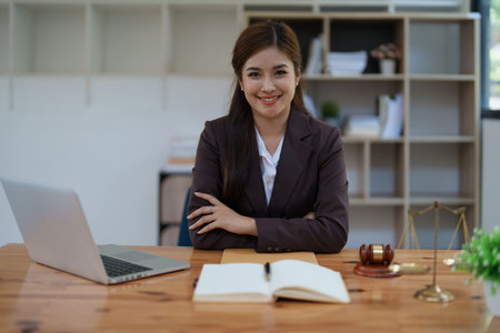 female attorney advisor at a law firm reviews legal documents at her desk equipped with a laptop notebook and scales of justice in the office.の写真素材