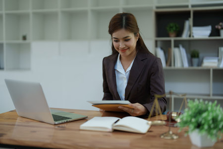 female attorney advisor at a law firm reviews legal documents at her desk equipped with a laptop notebook and scales of justice in the office.の写真素材