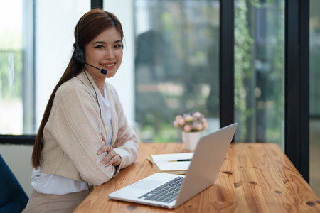 Asian businesswoman wears a headset while participation in an online video conference discussing marketing and finance strategies effectively.の写真素材