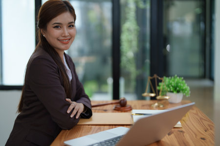 female attorney advisor at a law firm reviews legal documents at her desk equipped with a laptop notebook and scales of justice in the office.の写真素材