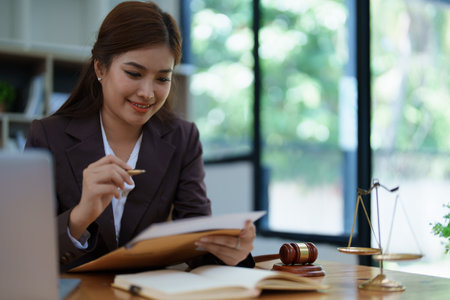 female attorney advisor at a law firm reviews legal documents at her desk equipped with a laptop notebook and scales of justice in the office.の写真素材