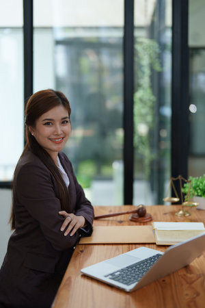 female attorney advisor at a law firm reviews legal documents at her desk equipped with a laptop notebook and scales of justice in the office.の写真素材