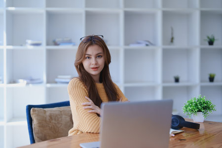 Smiling young woman engaged in online e-learning at her desk with a laptop notebook and headphones creating a positive study atmosphere for success.の写真素材