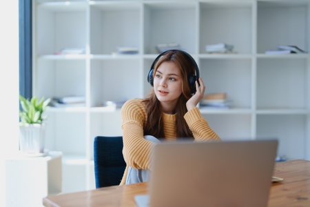 Young woman enjoying a relaxing music break at her desk while using headphones, writing in a notebook, and working on her laptop for calm inspiration.の写真素材