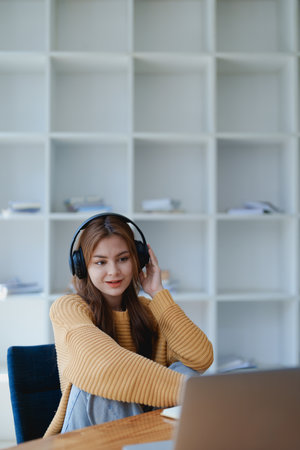 Young woman enjoying a relaxing music break at her desk while using headphones, writing in a notebook, and working on her laptop for calm inspiration.の写真素材