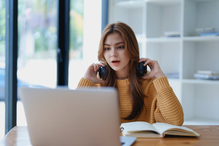 Young woman enjoying a relaxing music break at her desk while using headphones, writing in a notebook, and working on her laptop for calm inspiration.の写真素材
