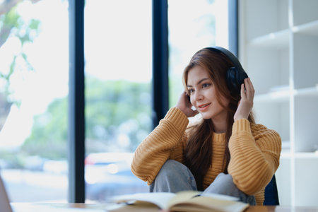 Young woman enjoying a relaxing music break at her desk while using headphones, writing in a notebook, and working on her laptop for calm inspiration.の写真素材