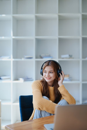 Young woman enjoying a relaxing music break at her desk while using headphones, writing in a notebook, and working on her laptop for calm inspiration.の写真素材