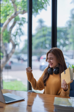 young woman happy, viewing her excellent success score in her e-learning program displayed on her laptop at her desk at home.の写真素材