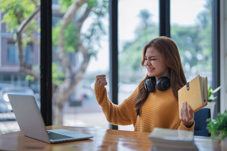 young woman happy, viewing her excellent success score in her e-learning program displayed on her laptop at her desk at home.の写真素材