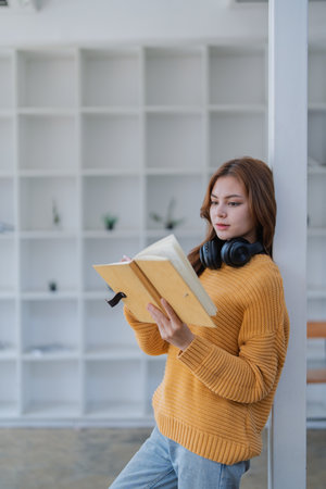 happy young woman with headphones is immersed in a book, happily learning.の写真素材